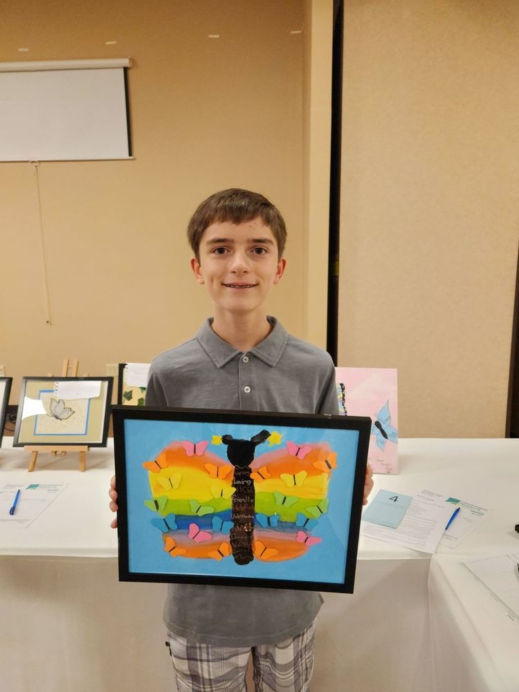 middle school student holds a piece of artwork of a colorful butterfly in rainbow colors and framed